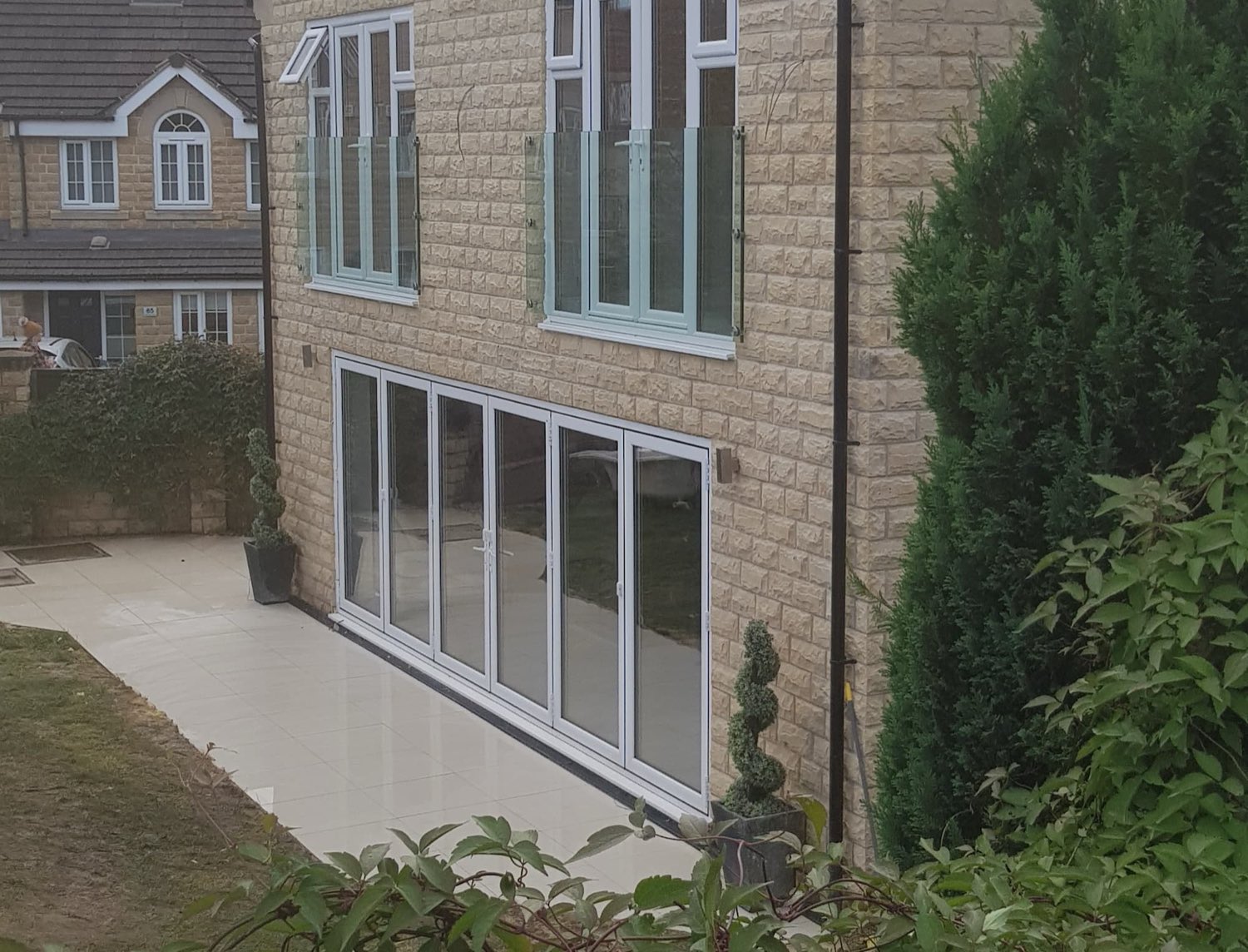 Stone-faced house extension with white bi-fold doors opening onto a tiled patio